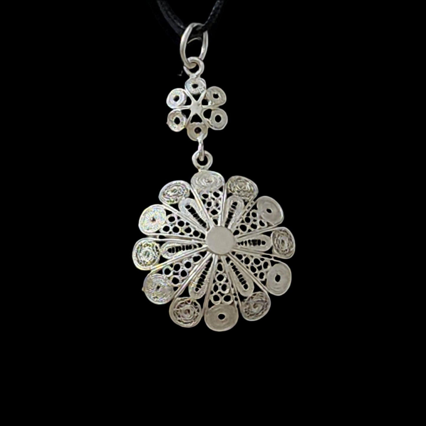 Back view of a sterling silver filigree pendant with intricate floral patterns and detailed craftsmanship, displayed against a black background.