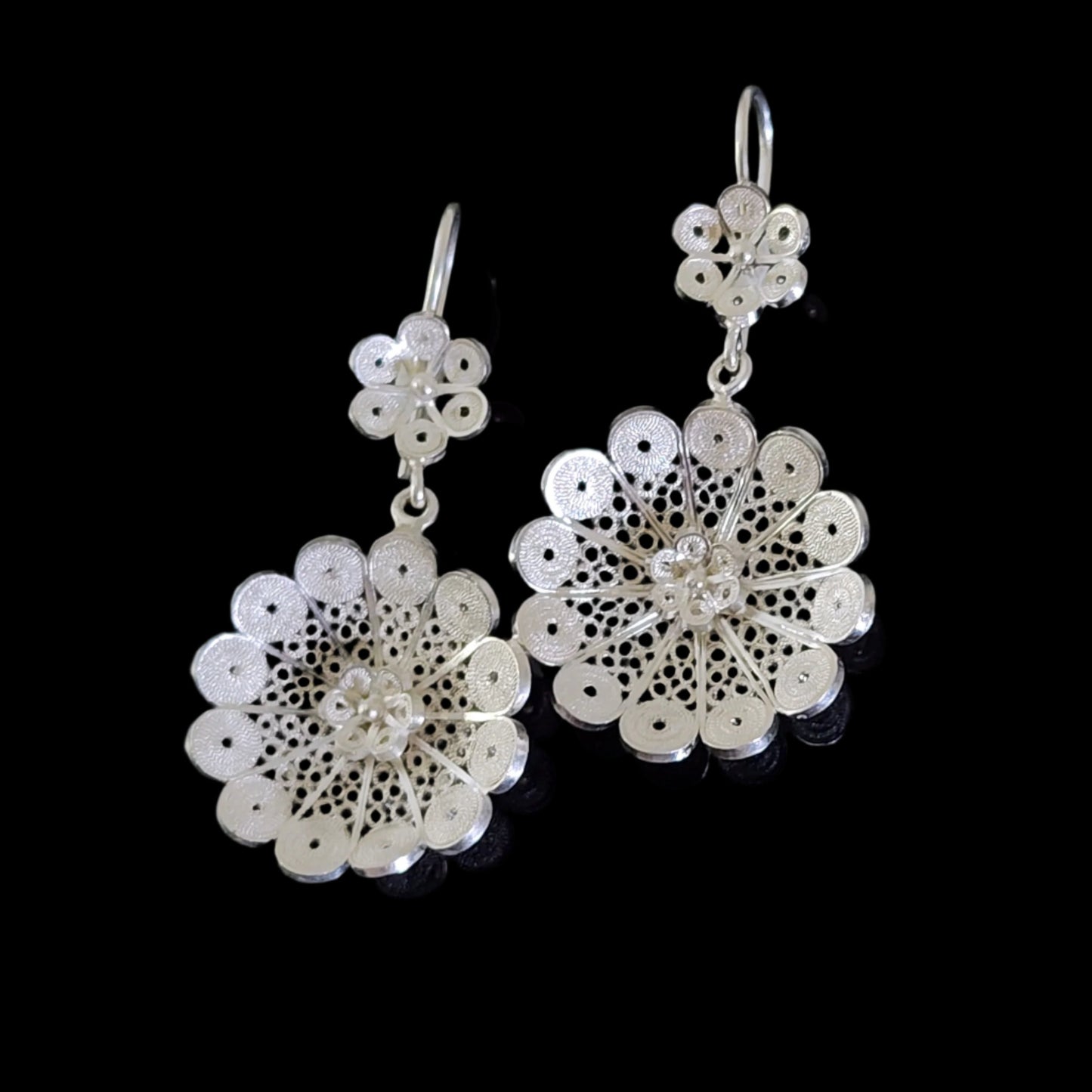 Intricate sterling silver filigree earrings with floral motifs and delicate drop design, displayed against a black background.