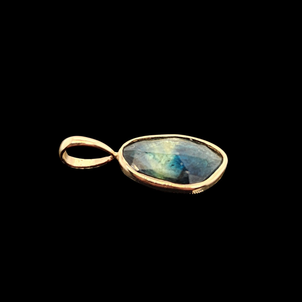 A side view of the rose-cut bi-color sapphire pendant, showcasing the shimmering stone in a 14kt gold bezel with a sleek gold bail, resting against a black background.