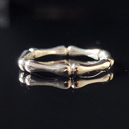 A silver ring with a bone-like, textured design on a reflective black background, showcasing its polished finish and organic, sculptural details.