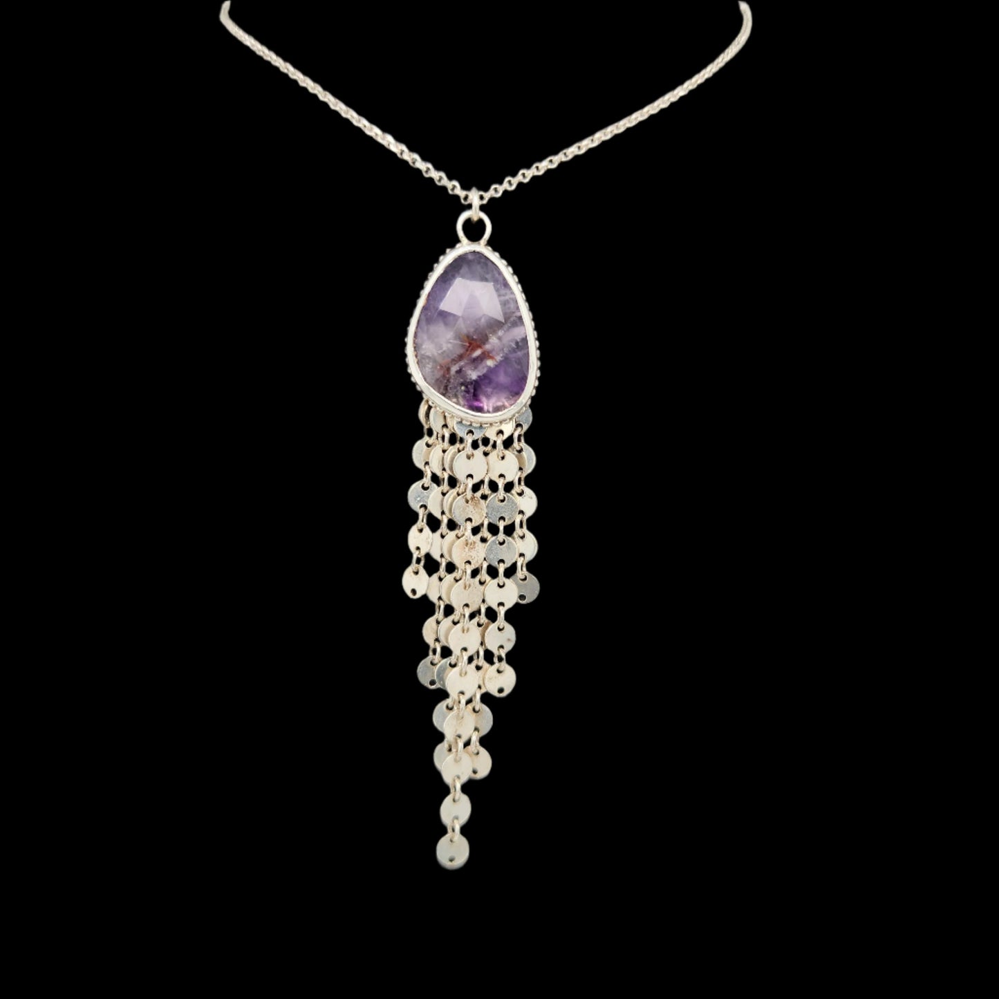 Elegant sterling silver necklace featuring a faceted teardrop-shaped amethyst pendant with cascading silver chain fringe, displayed against a black background.