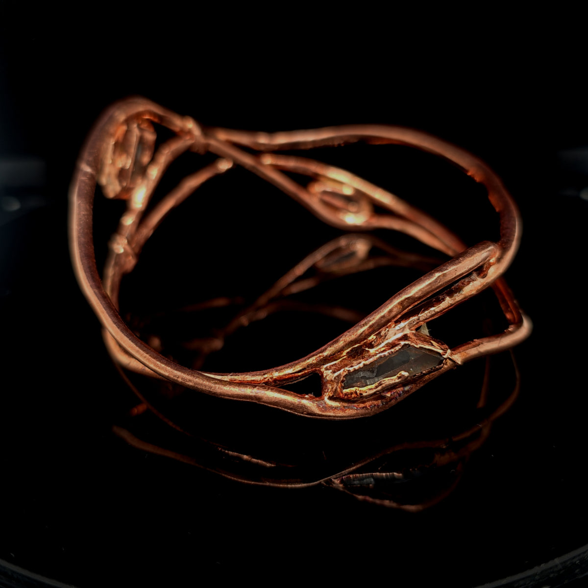 copper-toned wrap bracelet with raw, organic-shaped clear quartz gemstones, displayed on a reflective black surface.