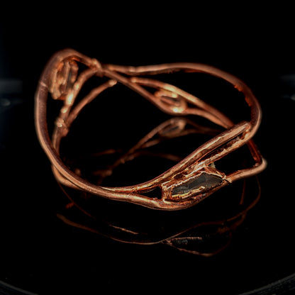 copper-toned wrap bracelet with raw, organic-shaped clear quartz gemstones, displayed on a reflective black surface.