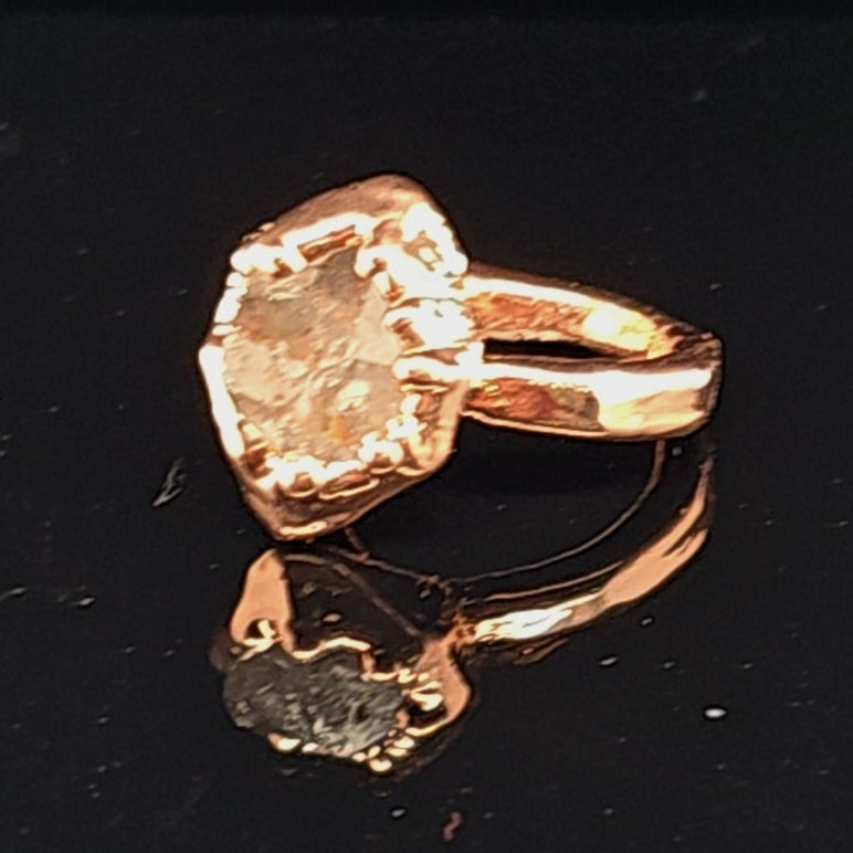A copper metallic ring with a flag band and with a large herkimer diamond that appears pale peach or champagne-colored due to the reflection of the pure copper on a black background.