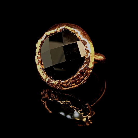 A copper ring with a large, rough-cut black gemstone, photographed on a reflective black surface.