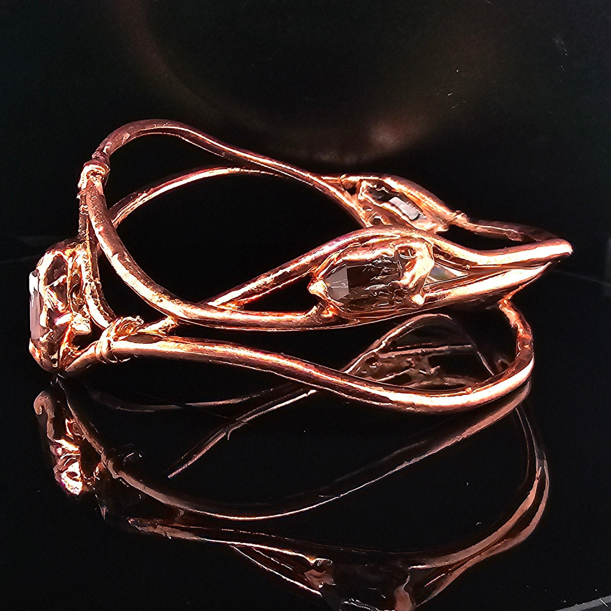 copper-toned wrap bracelet with raw, organic-shaped clear quartz gemstones, displayed on a reflective black surface.