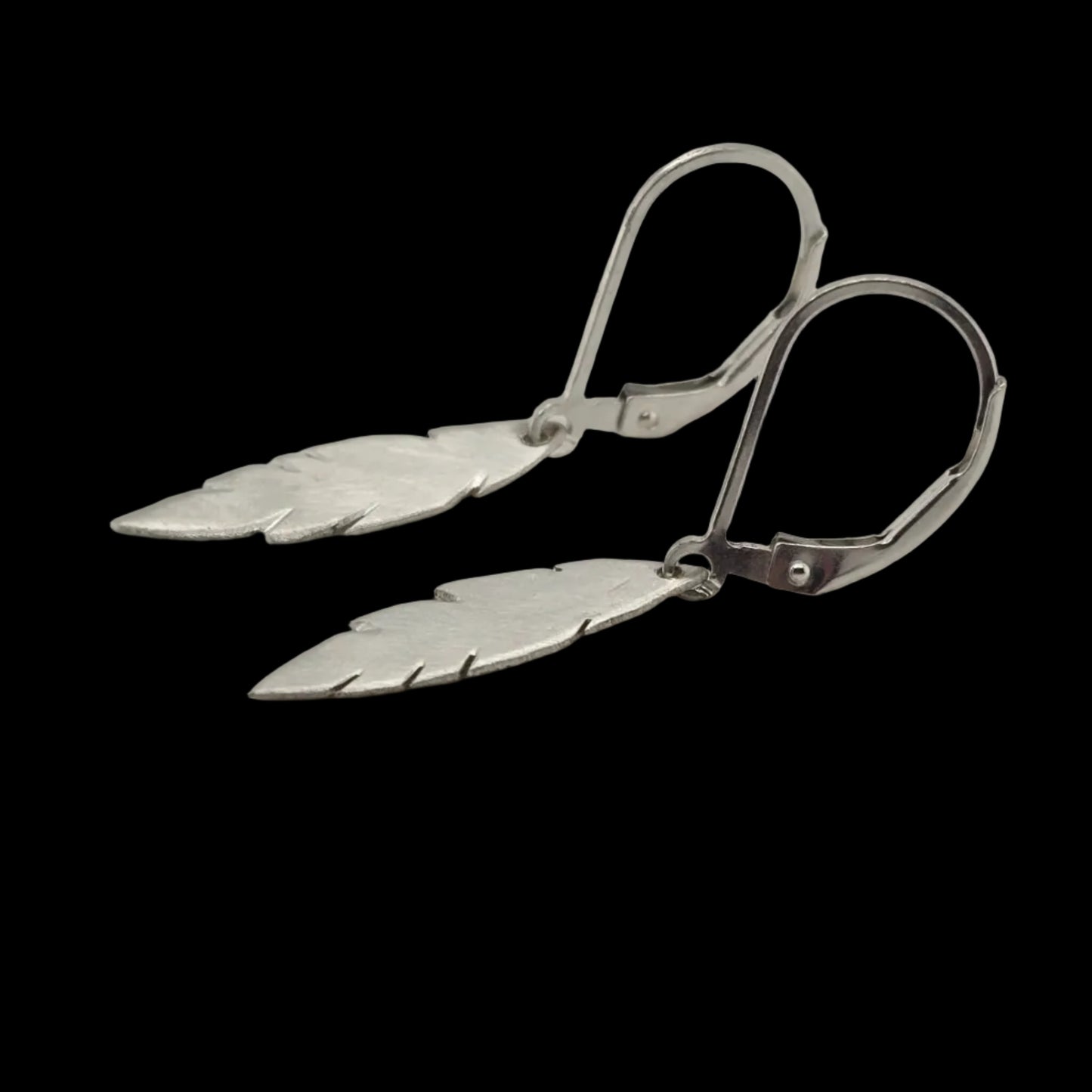 Pair of sterling silver feather drop earrings with a brushed finish, hanging from sterling silver leverback hooks on a black background.