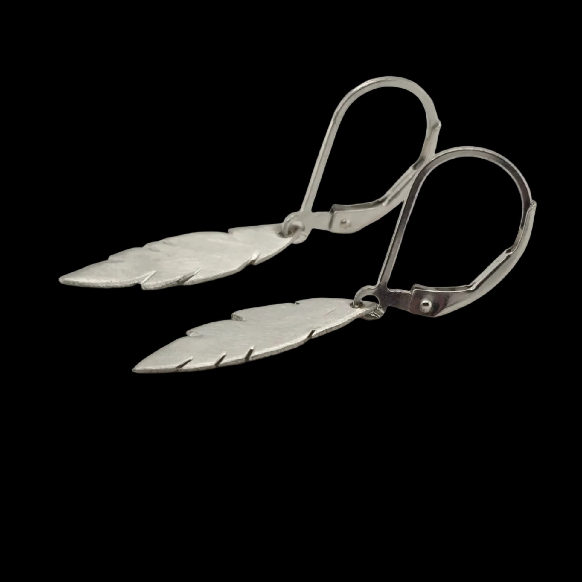 Pair of sterling silver feather drop earrings with a brushed finish, hanging from sterling silver leverback hooks on a black background.