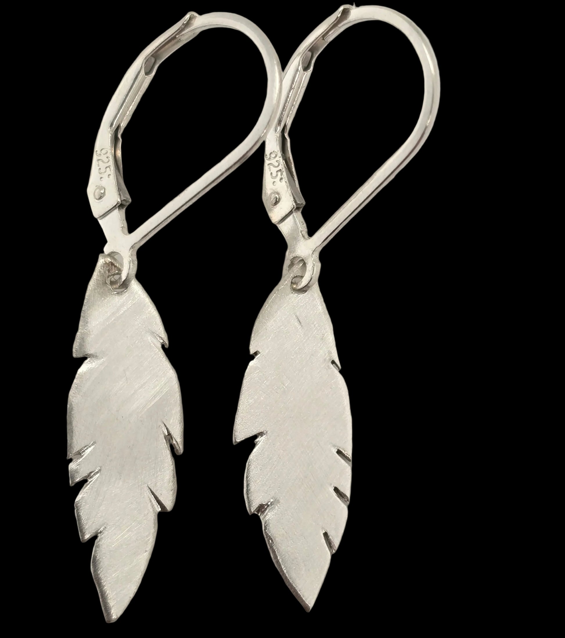 Pair of sterling silver feather drop earrings with a brushed finish, hanging from sterling silver leverback hooks on a black background.