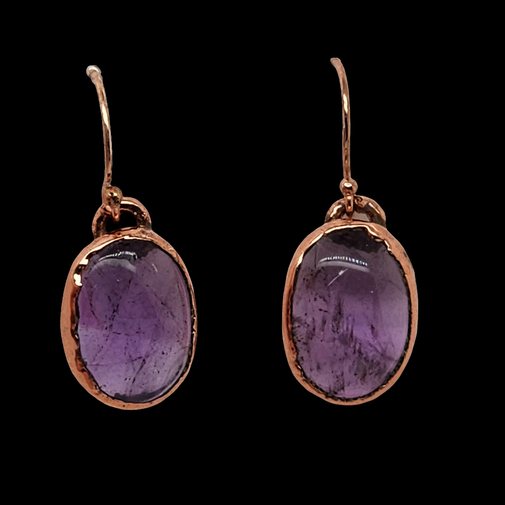 Handcrafted copper earrings featuring raw amethyst stones, displayed against a black background, showcasing their rustic and earthy design.