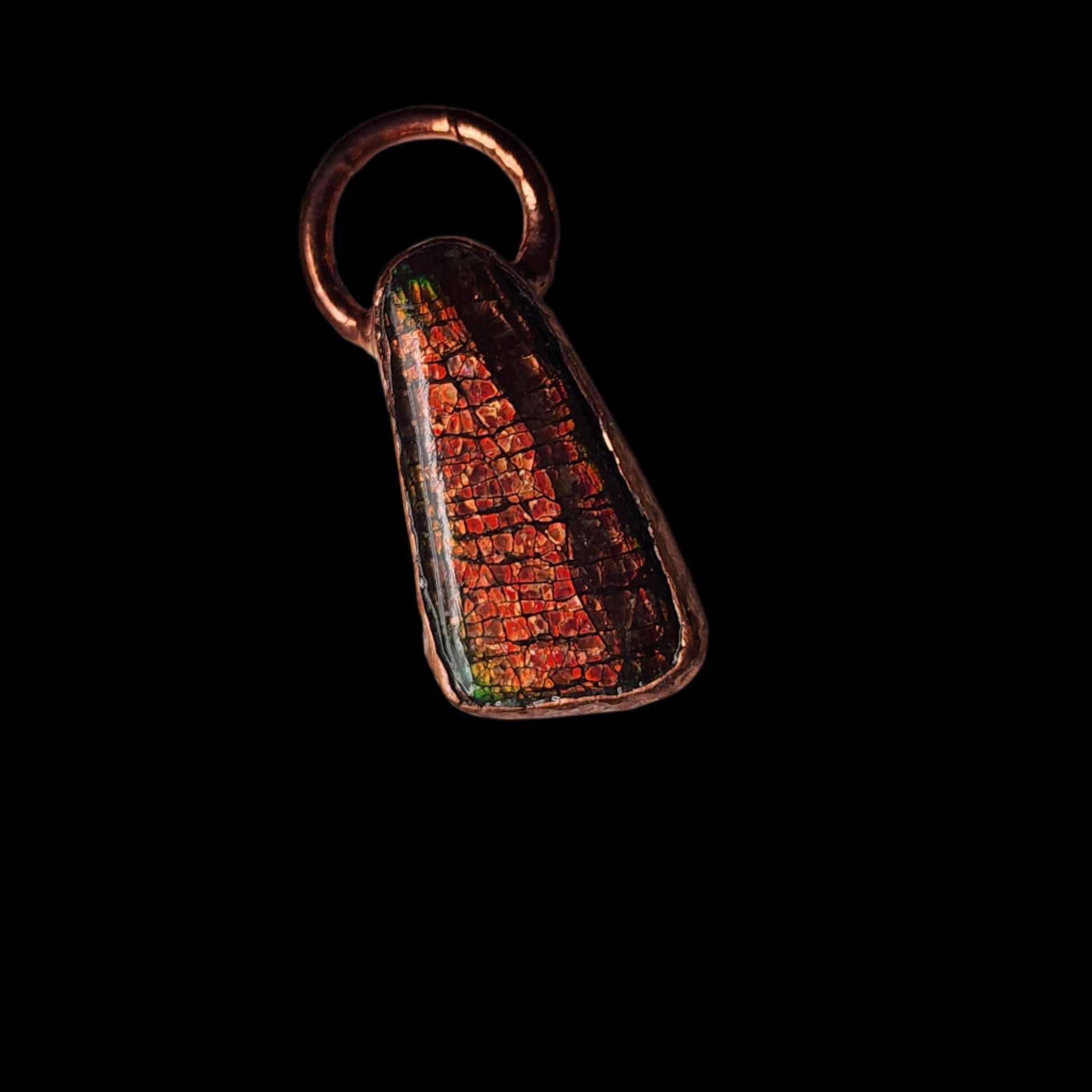 Copper pendant featuring a vibrant ammolite gemstone with fiery red, orange, and green hues, displayed on a black background. The gemstone showcases a natural iridescent mosaic pattern.