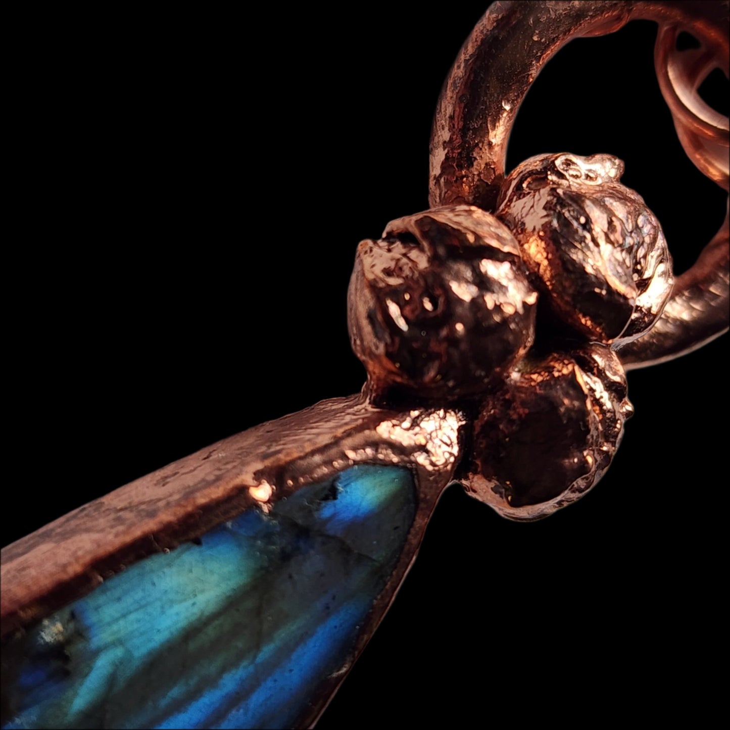 Angled close-up of the copper labradorite pendant, highlighting the textural details of the buds and the gemstone's luminous blue-green hues.