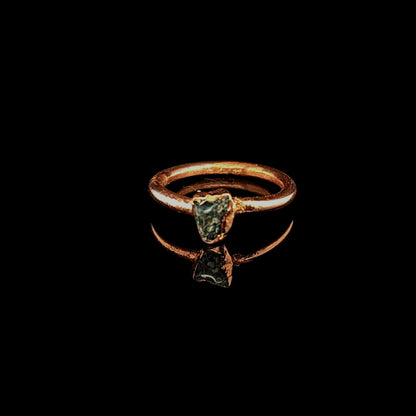 A rustic copper ring featuring a triangular teal apatite stone, displayed on a reflective black surface.