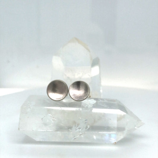 Round, Brushed Concave Circular Sterling Silver Lunar Studs sit on Top of A Crystal with another Crystal in the Background. They softly reflect the light, like the moon, hence the name "lunar studs"