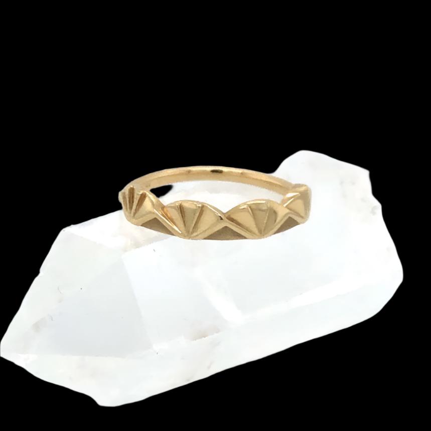 Minimalist 14kt gold ring featuring a geometric fan-inspired design, displayed on a white crystal point, against a black background.